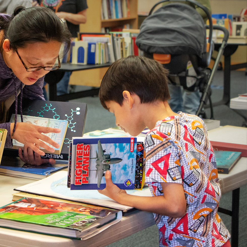Adult and child looking at books on a table in a library.