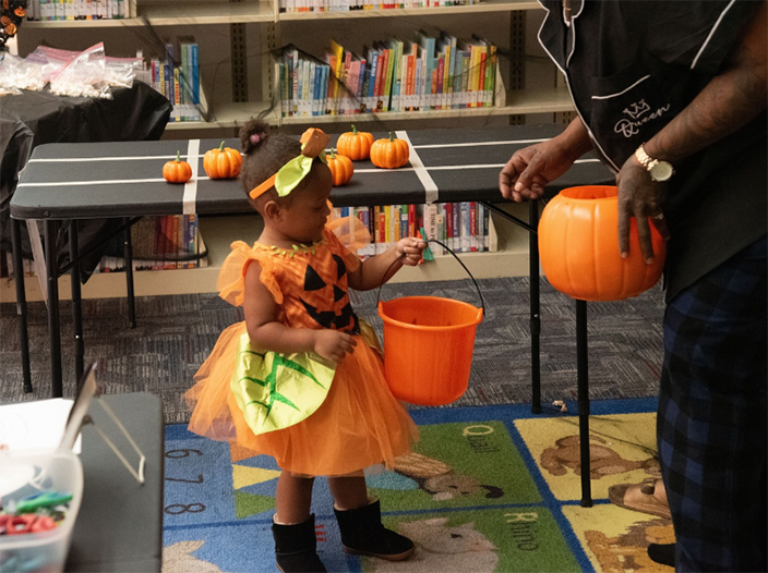 A little girl wearing a pumpkin Halloween costume and holding an orange bucket