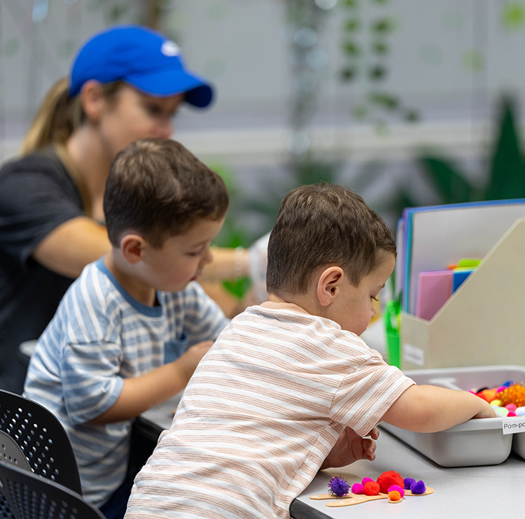 Two young boys do a craft activity  at a recreation center table.